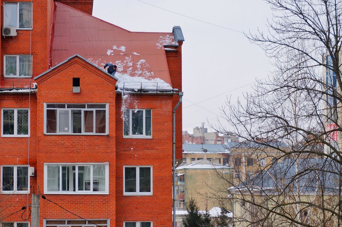 A man cleaning snow on the roof of a multi-storey residential building in the city of Voronezh, Russia